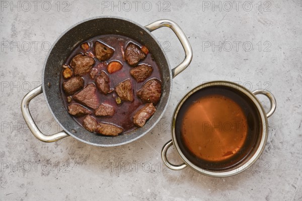 Chunks of tender beef and vegetables are slow-cooked in a pot, creating a hearty stew with dark broth. A separate pot contains a clear beef broth, both ready for a comforting meal