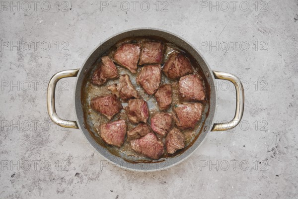 Chunks of beef are sizzling in a frying pan, showcasing a delicious golden-brown crust in the kitchen countertop