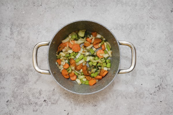 Chopped carrots, celery, and onion are frying in a pot, creating a vibrant vegetable base mixture on kitchen tabletop