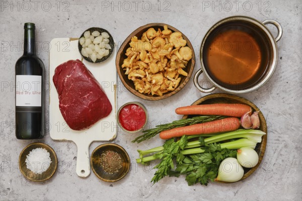 Fresh vegetables and tender beef are arranged on a kitchen counter, preparing for a delicious stew. Ingredients include carrots, celery, onions, and a bottle of red wine, ready for cooking