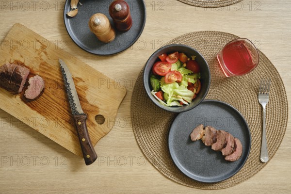 Slices of succulent duck breast are laid out on a cutting board beside a vibrant salad filled with tomatoes and lettuce. A refreshing drink sits nearby, creating an inviting dining experience