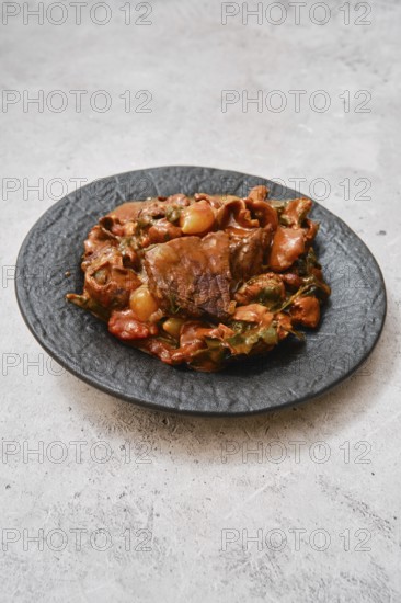 A hearty meat stew is presented on an elegant black plate. The dish features tender chunks of beef cooked with assorted colorful vegetables in a savory mushroom sauce, highlighting rich aromas and flavors
