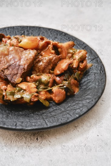 A flavorful combination of tender meat and a medley of vegetables on a black plate. The dish displays rich colors, hinting at a satisfying meal perfect for any dining occasion