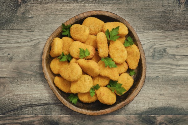 A generous serving of golden chicken nuggets is arranged in a rustic wooden bowl, garnished with fresh herbs. This dish offers a delicious snack or meal option perfect for gatherings