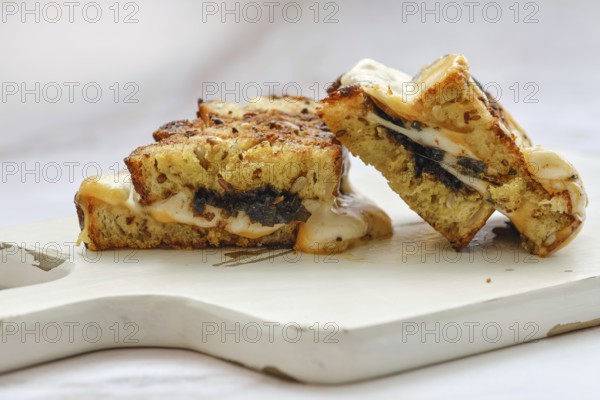 A delicious three cheese sandwich sits on a wooden cutting board, showcasing a golden-brown crust. Melted cheese oozes from the sides, indicating fresh preparation. Perfect for lunchtime