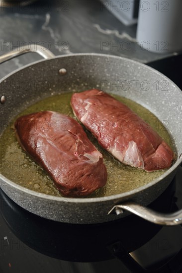 Two duck breasts are sizzling in a pan with hot fat, infusing the kitchen with rich aroma