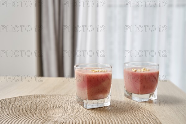 Two glasses filled with a vibrant banana-strawberry smoothie are placed on a light wooden table