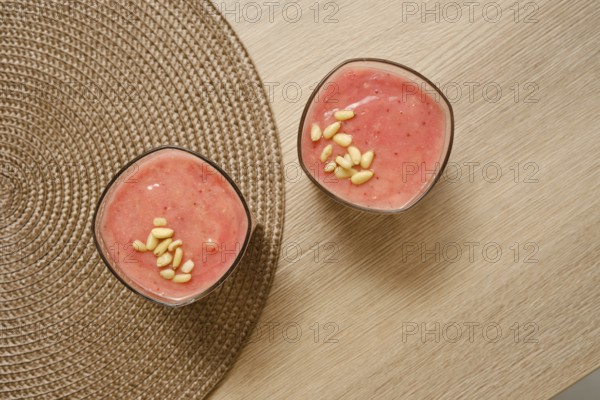 Two glasses filled with a creamy banana-strawberry smoothie sit on a natural-colored table. Topped with pine nuts, this refreshing drink is perfect for a healthy breakfast or snack