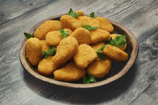 A generous portion of golden chicken nuggets is neatly arranged in a wooden bowl, garnished with fresh green herbs