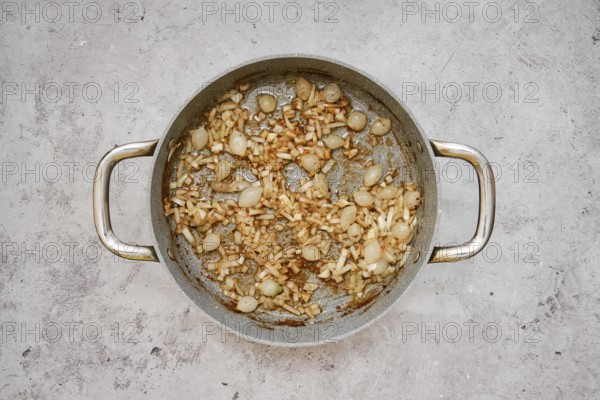 A silver pan contains a mixture of caramelized pearl onions and chopped shallot, creating a savory aroma in the kitchen. The onions are golden brown, indicating a rich flavor