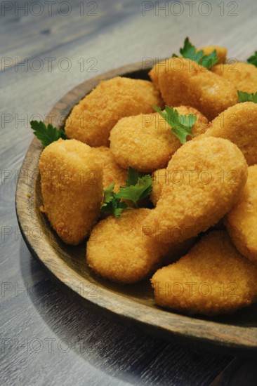 Close-up view of golden-brown chicken nuggets in breading on a rustic wooden platter. The crispy pieces are garnished with fresh parsley, perfect for sharing at any meal or gathering