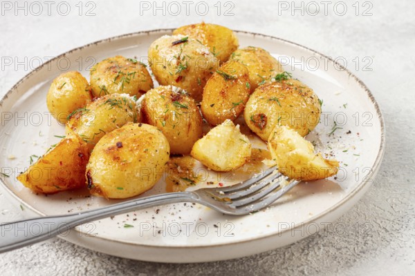 Half-eaten fried new potatoes, with butter and dill, on a white plate, with a fork, at home, no people