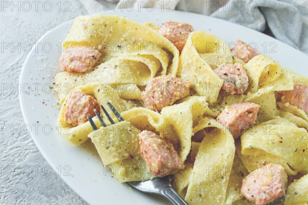 Papardelle pasta, in creamy sauce with salmon, natural light, lifestyle, homemade, on a gray background, no people