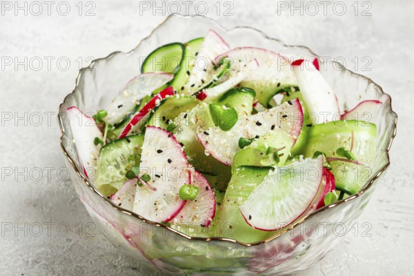 A vibrant vegetable salad is prepared with slices of radishes and cucumbers, garnished with herbs and seasoned with pepper. The dish is presented in a decorative glass bowl