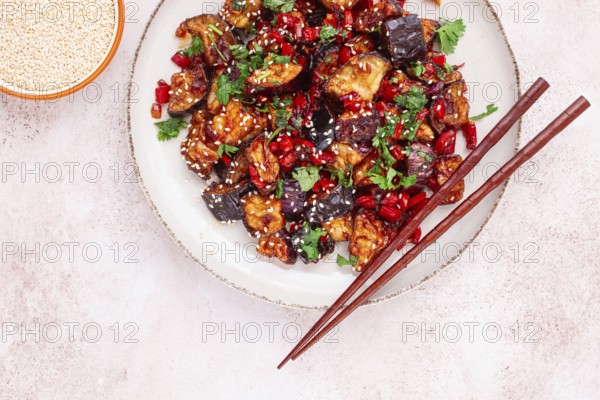 Fried eggplant, Chinese style, in sweet and sour sauce, with pepper and sesame seeds. on a white plate