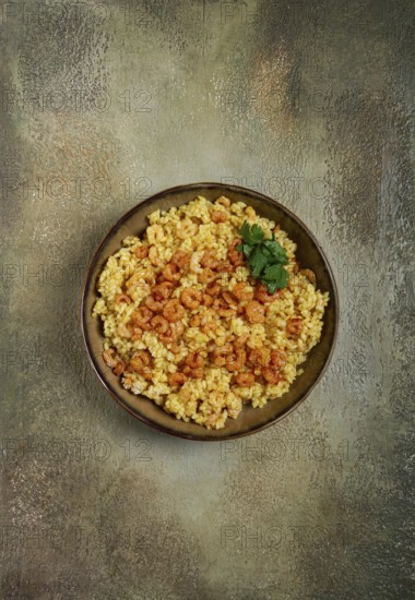 Risotto with shrimp, in a bowl, on a textured surface, with a side dish of fresh coriander, homemade, no people