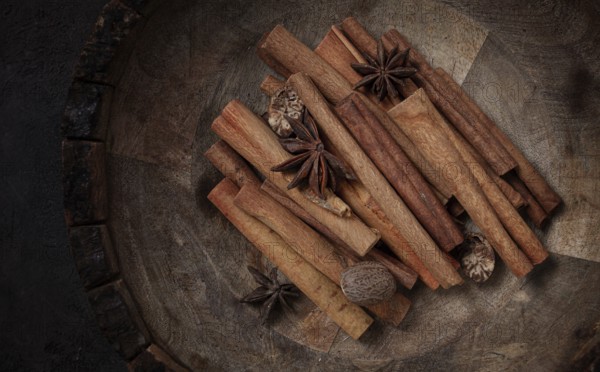 Cinnamon sticks, with nutmeg and anise star, in a wooden plate, top view, no people