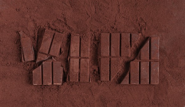 Chocolate bars broken and scattered on cocoa powder background with rich texture and color