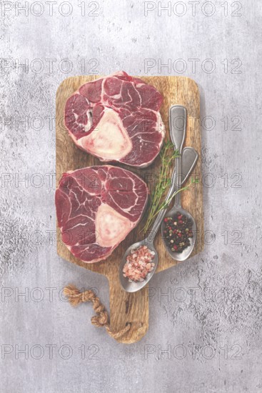 Freshly sliced beef legs, two ossobuco steaks, on a wooden board, with spices and herbs, ready to cook