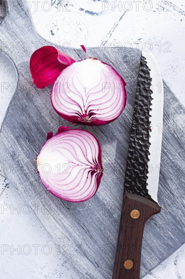 A vibrant red onion is cut in half, on a rustic wooden chopping board beside a sharp knife, ready for cooking