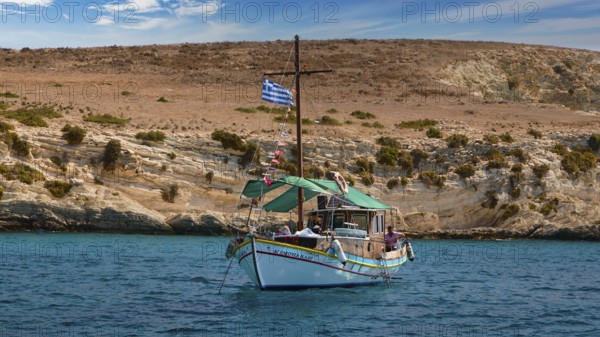 A boat with a Greek flag sails along rocky shores, the sea is blue and calm, White Cliffs, White Beach, Makri Aspronisi Island, Natura 2000 area, boat trip, Aspronisi, Lipsi, Dodecanese, Greek Islands, Greece