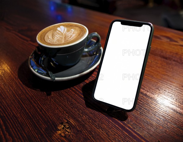 A sleek mobile phone placed near a cup of coffee, set against a blurred, warm glowing lights background, creating a cozy and modern scene perfect for technology and relaxation themes, AI generated