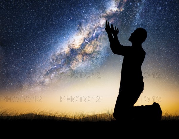 A man kneels in peaceful reflection under the vibrant Milky Way galaxy at sunset in an open natural setting, making prays, AI generated
