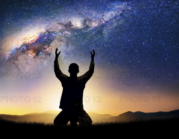 A man kneels in peaceful reflection under the vibrant Milky Way galaxy at sunset in an open natural setting, making prays, AI generated
