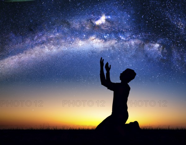 A man kneels in peaceful reflection under the vibrant Milky Way galaxy at sunset in an open natural setting, making prays, AI generated