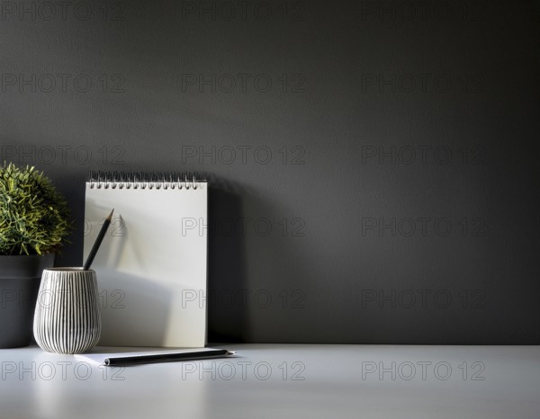 A clean and modern office workspace featuring a pen holder, notebook, and ceramic vase against a dark wall, AI generated