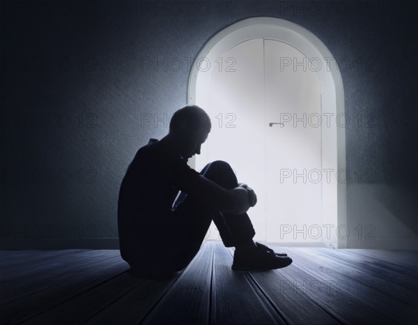 A silhouette of a person seated on the floor, conveying feelings of sadness and solitude against a softly lit window in a quiet place, AI generated