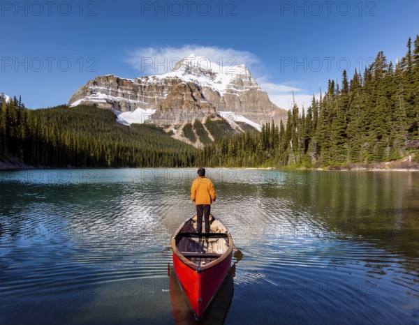 A serene moment of solitude depicted as an individual rows a boat across a tranquil mountain lake surrounded by lush forests and breathtaking peaks under a clear blue sky, AI generated
