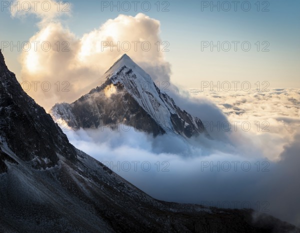 A stunning view of a snowy mountain peak rising above the clouds, with a blue sky background. Capturing a tranquil moment in nature's beauty, evoking feelings of serenity and wonder, AI generated