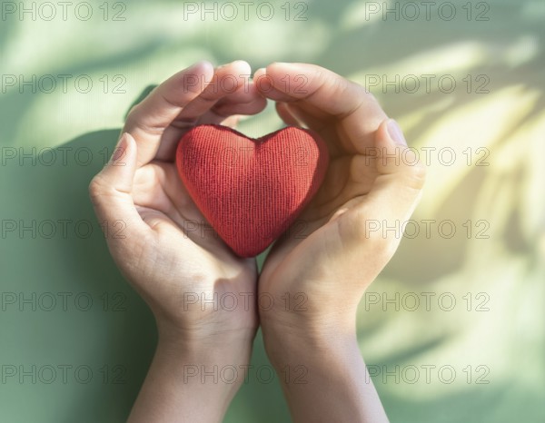 A pair of hands gently holding a red fabric heart, conveying themes of love, care, and compassion. The soft textures and muted background emphasize heartwarming emotions in the image, AI generated