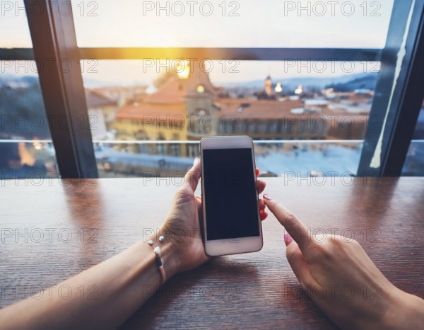 A person holding a smartphone at an outdoor cafe amidst a vibrant and lively urban setting. The image captures a relaxed moment with modern technology interaction and a scenic cityscape, AI generated