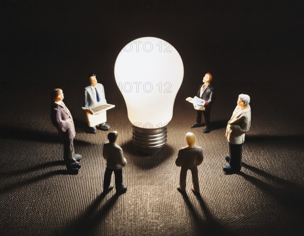 Miniature people standing around a glowing light bulb symbolizing creativity, teamwork, and innovative ideas in a business setting, AI generated