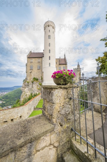 A tall tower with pink flowers in a stone wall arrangement in front of a castle, Lichtenstein Castle, Lichtenstein, Swabian Alb, Germany