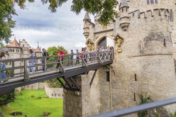 Group of tourists crossing a historic wooden bridge at a majestic castle gate, Lichtenstein Castle, Lichtenstein, Swabian Alb, Germany