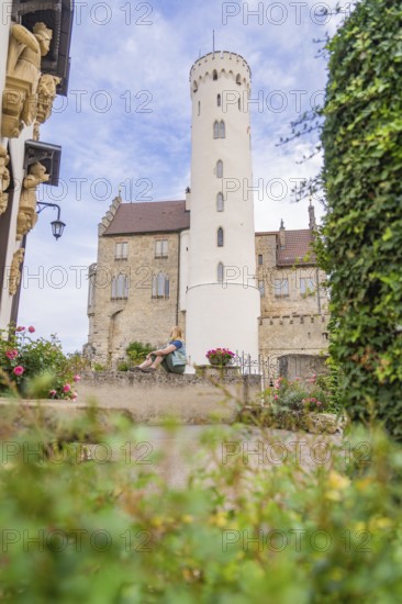 Woman sitting quietly in a castle garden in front of a high tower, Lichtenstein Castle, Lichtenstein, Swabian Alb, Germany