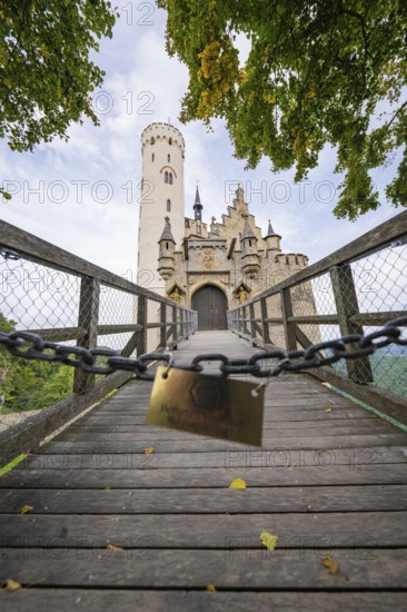A bridge leads to a majestic Gothic-style castle surrounded by autumnal trees, Lichtenstein Castle, Lichtenstein, Swabian Alb, Germany