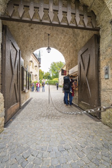 People pass a large wooden stone gate leading to a castle, Lichtenstein Castle, Lichtenstein, Swabian Alb, Germany