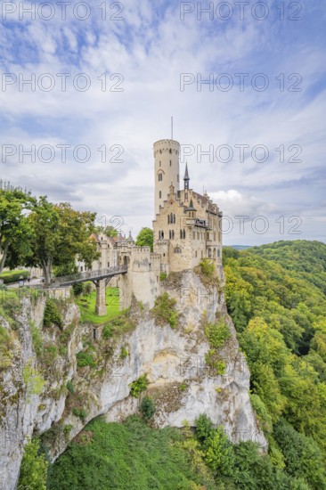 Medieval castle with high tower on a rocky outcrop surrounded by lush green forests and dramatic skies, Lichtenstein Castle, Lichtenstein, Swabian Alb, Germany