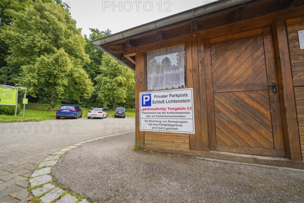 A small car park with a wooden hut and parked cars at the edge of the forest, Lichtenstein Castle, Lichtenstein, Swabian Alb, Germany