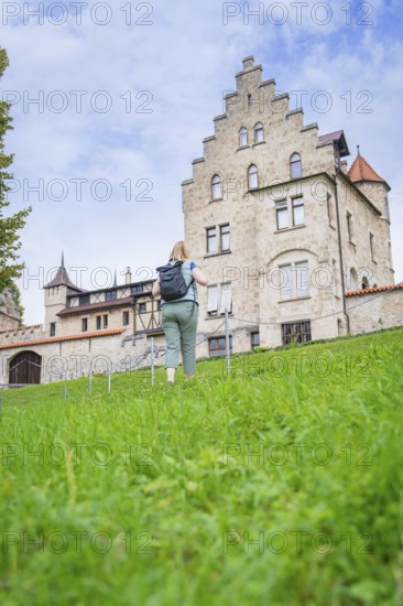 A woman walks up a grassy hill towards an imposing historic castle, Lichtenstein Castle, Lichtenstein, Swabian Alb, Germany