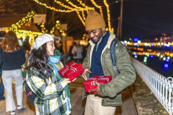Young multiethnic couple exchanging christmas gifts at a christmas market, enjoying winter holidays together
