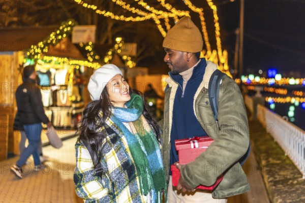 Happy multi ethnic couple enjoying christmas time together, exchanging gifts at a magical christmas market