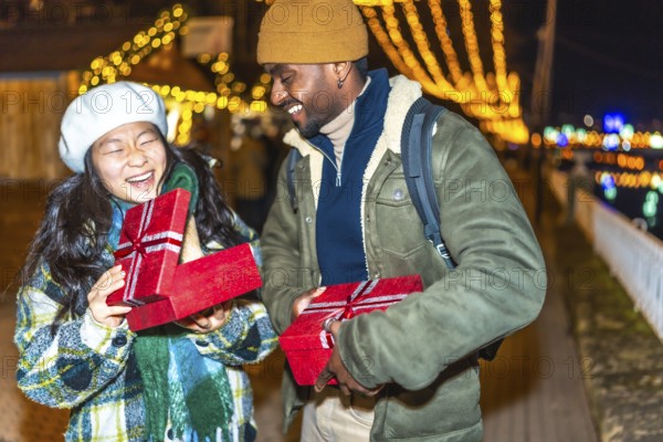 Young multiethnic couple exchanging christmas gifts at a christmas market, enjoying the festive atmosphere and holiday spirit