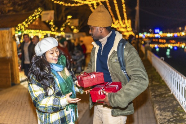 Happy multiethnic couple exchanging christmas gifts at a christmas market, enjoying winter holidays and christmas spirit