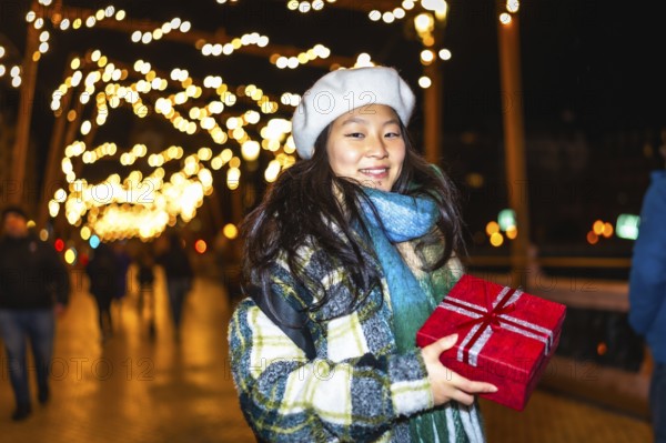 Young asian woman holding red christmas gift enjoying christmas lights decoration at night in the city
