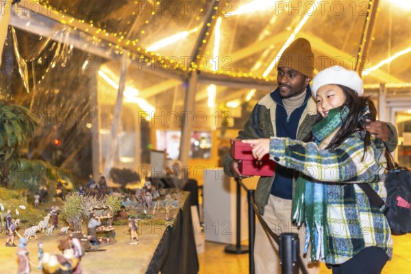 Happy multiethnic couple holding christmas gifts and enjoying a nativity scene exhibition